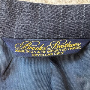 May include: A dark blue pinstripe suit jacket with a gold label that reads "Brooks Brothers Made in U.S.A. of Imported Fabric Dry Clean Only."