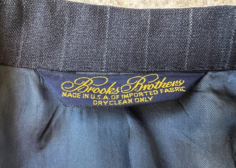May include: A dark blue pinstripe suit jacket with a gold label that reads "Brooks Brothers Made in U.S.A. of Imported Fabric Dry Clean Only."
