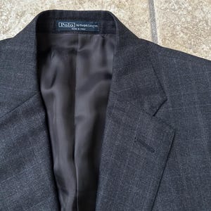 May include: A dark gray blazer with a subtle textured pattern. The label reads "Polo by Ralph Lauren" and "Made in Italy".