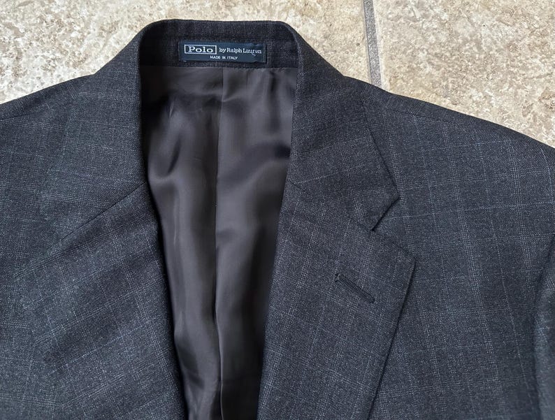May include: A dark gray blazer with a subtle textured pattern. The label reads "Polo by Ralph Lauren" and "Made in Italy".