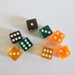May include: A collection of seven colorful dice. The dice are in various colors, including brown, green, and orange. Each die has white dots indicating the numbers. The dice are scattered on a white surface.