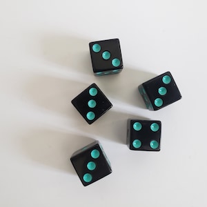 May include: Five black dice with turquoise dots. Each die has a different number of dots, ranging from two to six.