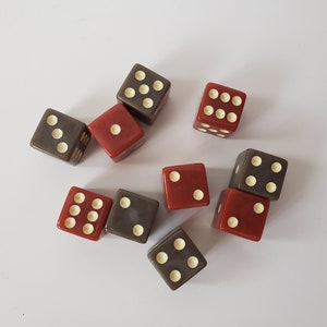 May include: A collection of ten dice, some red and some gray, with white dots on each face. The dice are arranged in a random pattern on a white surface.