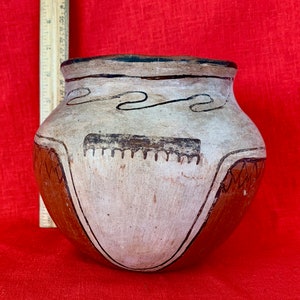 May include: A white ceramic pot with brown and black painted designs. The pot has a rounded body and a wide opening.