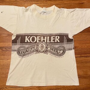 May include: White t-shirt with a brown print of a beer label that reads "Kofhler Family Brewing Since 1847 Quality Beer. Once Genuine Erie Brewing. Products Bear This Seal."