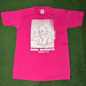 May include: Pink t-shirt with a white graphic of a baby lion with a butterfly. The text "GIRL SCOUTS" and "CORRY, PA" is printed below the image.