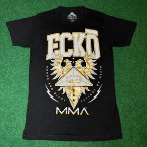 May include: Black t-shirt with a gold and white graphic print of a stylized eagle with the text "ECKO" and "MMA" on the front. The graphic also includes the text "Honor and Glory" and "Victory or Death".