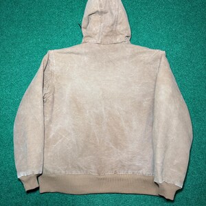 Puede incluir: Chaqueta con capucha de color beige con cord&oacute;n, pu&ntilde;os y cintura de canal&eacute;. La chaqueta est&aacute; hecha de un material duradero y desgastado, y la capucha est&aacute; sujeta a la espalda.