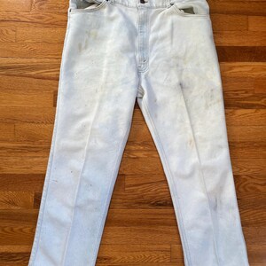 May include: Light blue denim jeans with a faded appearance and visible wear and tear. The jeans have a straight leg and a classic five-pocket style.
