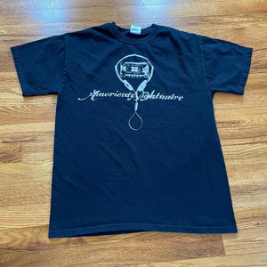 May include: Black t-shirt with a white graphic of a cassette tape with headphones and the text "American Nightmare".