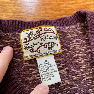 May include: A brown and tan knit cardigan with a label that reads "Heirloom Collectibles" and "Design and Pattern Copyrighted 1996". The label also includes the size "XL" and the fabric content: 54% ramie, 44% cotton, 2% other fiber. The cardigan was knitted in China and linked and looped in Hong Kong.