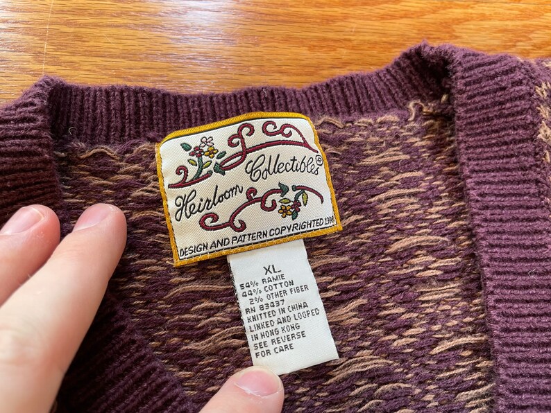 May include: A brown and tan knit cardigan with a label that reads "Heirloom Collectibles" and "Design and Pattern Copyrighted 1996". The label also includes the size "XL" and the fabric content: 54% ramie, 44% cotton, 2% other fiber. The cardigan was knitted in China and linked and looped in Hong Kong.