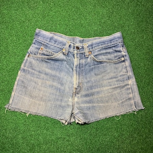 Peut inclure: Short en jean bleu clair avec ourlet effiloché. Le short a une coupe classique à cinq poches, une fermeture boutonnée et zippée, et des passants de ceinture. Le denim a un aspect délavé et usé.