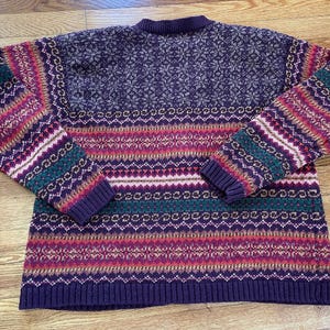 May include: A purple, green, pink, and white striped sweater with a snowflake pattern on the top.