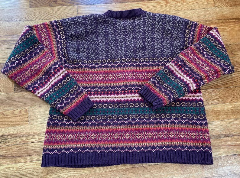 May include: A purple, green, pink, and white striped sweater with a snowflake pattern on the top.