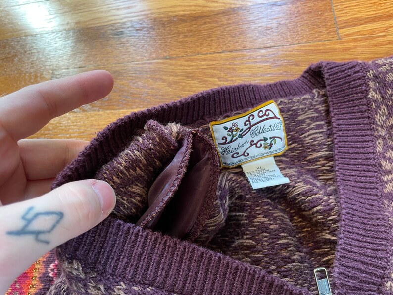 May include: A brown and beige patterned sweater with a V-neck and a zipper. The sweater has a label that reads "Heirloom Collectibles".
