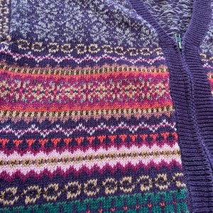 May include: Purple, pink, green, and white knitted cardigan with a zipper closure. The cardigan has a fair isle pattern with gold thread accents.