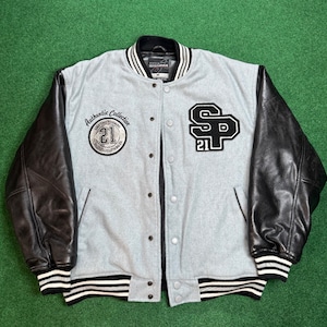 May include: A gray and black varsity jacket with leather sleeves. The jacket has a white stripe around the collar and cuffs. The front of the jacket has a patch with the text "Authentic Collection" and the number "21". The back of the jacket has a patch with the letters "SP" and the number "21".