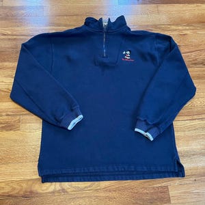 Può includere: Una felpa blu navy con zip a un quarto con un motivo di Topolino e il testo "Walt Disney World" ricamato sul petto.