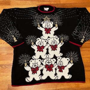 Könnte beinhalten: Schwarzer Weihnachtspullover mit einem weißen Teddybär-Weihnachtsbaum-Design. Die Bären halten Funken und tragen rote Schleifen. Der Pullover hat einen roten Saum an Hals und Ärmeln.