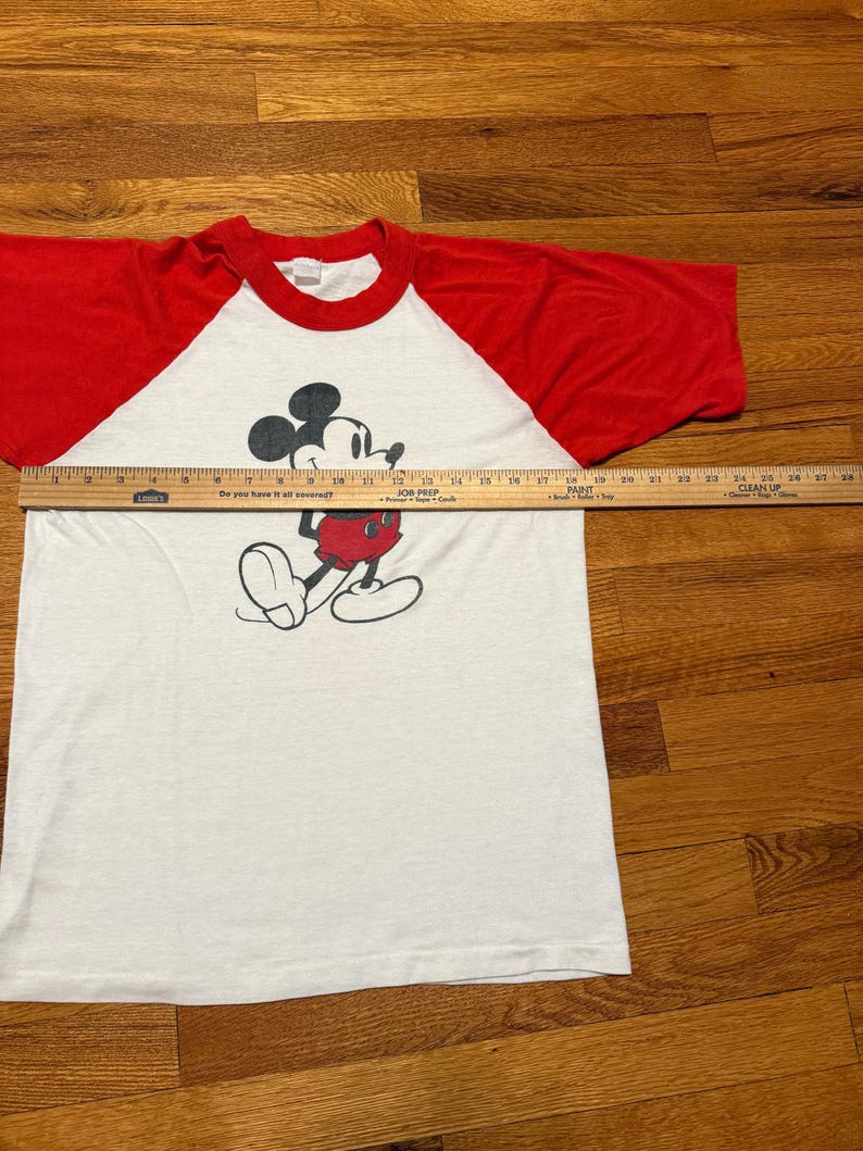 Pu&ograve; includere: T-shirt bianco e rosso a maniche raglan con grafica di Topolino. La grafica mostra Topolino in nero, rosso e bianco. La maglietta misura circa 71 cm di lunghezza.