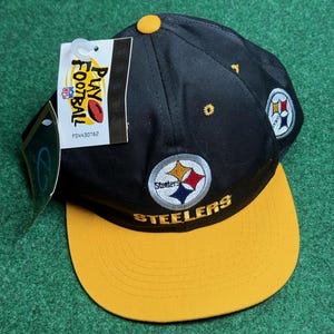 May include: Black and yellow Pittsburgh Steelers baseball cap with a team logo and the word "Steelers" embroidered on the front. The cap has a yellow brim and a black crown.