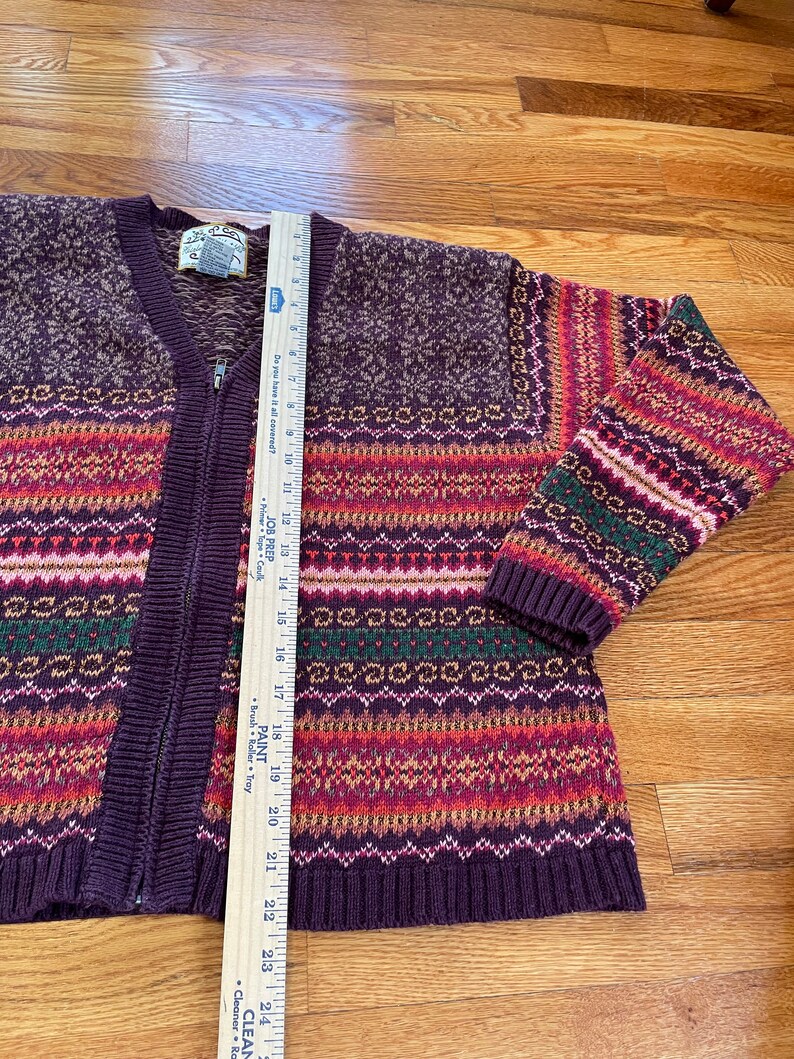 May include: A purple, red, green, and white striped cardigan sweater with a zipper closure. The sweater has a fair isle pattern and is made of a soft, knitted fabric.