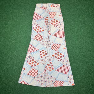 May include: White, patchwork-style pants with a flared leg. The pants feature a pattern of red polka dots, butterflies, and floral designs on a light blue and white background. The pants are made of a lightweight fabric.