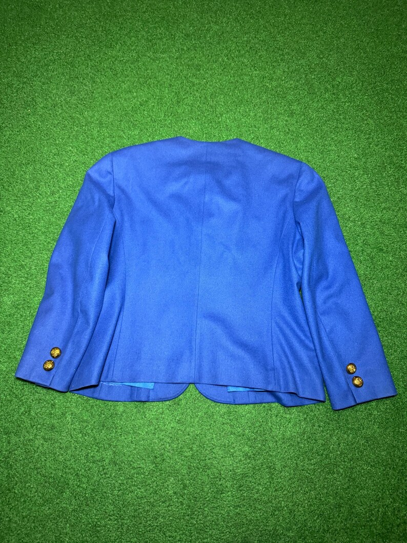 May include: A vibrant royal blue blazer with gold buttons. The back view highlights the tailored cut and button placement on the sleeves. The jacket is made from a smooth, possibly wool, fabric.
