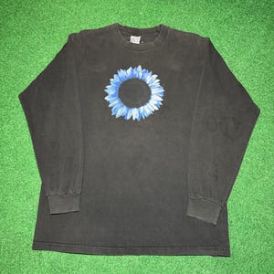May include: Black long-sleeve shirt featuring a blue and white floral design on the front. The shirt has a crew neck and long sleeves with ribbed cuffs. The shirt is made of a soft, comfortable material.