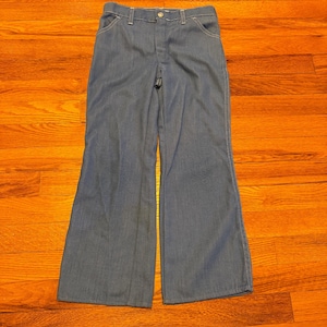May include: Blue denim bell-bottom pants with white stitching details. The pants have a button and zipper closure and front and back pockets. The pants are made of a medium-weight denim fabric.