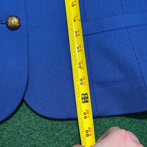 May include: A royal blue blazer with a gold button. The blazer is being measured with a yellow tape measure. The measurement is approximately 66 cm.