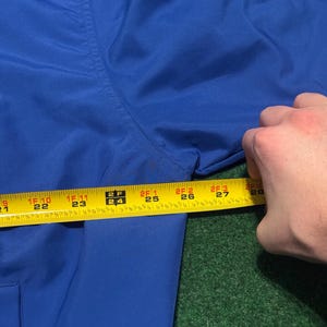 以下が含まれることがあります： ロイヤルブルーの衣服のクローズアップと黄色の巻尺。テープは56cmから71cmの測定値を示しています。衣服は緑色の表面にあります。