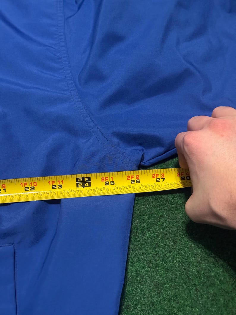 以下が含まれることがあります： ロイヤルブルーの衣服のクローズアップと黄色の巻尺。テープは56cmから71cmの測定値を示しています。衣服は緑色の表面にあります。