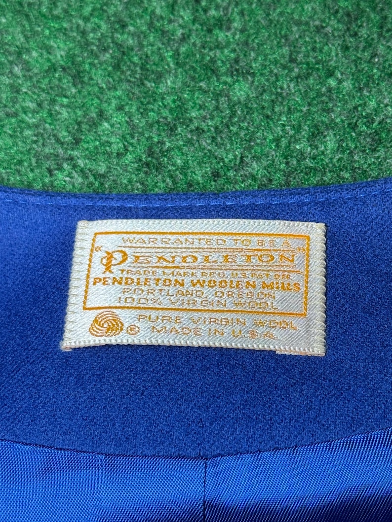 May include: Close-up of blue fabric with a cream-coloured label. The label has gold lettering and reads "PENDLETON WOOLEN MILLS" and "PURE VIRGIN WOOL". It also states "MADE IN U.S.A."