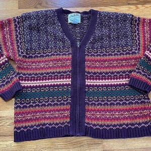 May include: A purple, green, pink, and white striped cardigan sweater with a zipper closure. The sweater has a fair isle pattern.