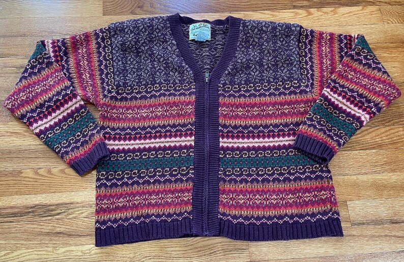 May include: A purple, green, pink, and white striped cardigan sweater with a zipper closure. The sweater has a fair isle pattern.