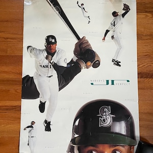 May include: A vintage Seattle Mariners baseball poster featuring a player in a white and green uniform with the text "Nobody's Perfect" and the team logo. The poster has a green and white colour scheme.