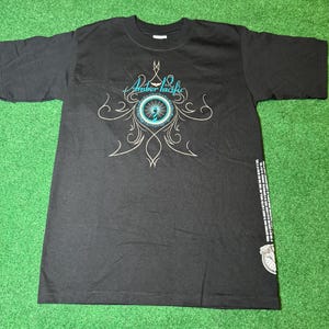 Pode incluir: Camiseta preta com um design gráfico azul e branco com o texto "Amber Pacific" e um padrão floral estilizado.