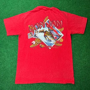 May include: Red t-shirt with a graphic of a person surfing with the text "Ron Jon Surf Shop Cocoa Beach" printed on the back.