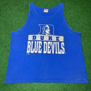 Peut inclure: Un débardeur bleu avec l'inscription "DUKE BLUE DEVILS" en lettres blanches. Au-dessus du texte se trouve un logo avec une figure de diable. Le débardeur est fait d'une matière douce et est sans manches.