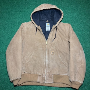 Puede incluir: Chaqueta con capucha marr&oacute;n con forro interior negro. La chaqueta tiene cierre de cremallera, dos bolsillos delanteros y dobladillo y pu&ntilde;os de canal&eacute;. El logotipo de Carhartt es visible en el bolsillo delantero.