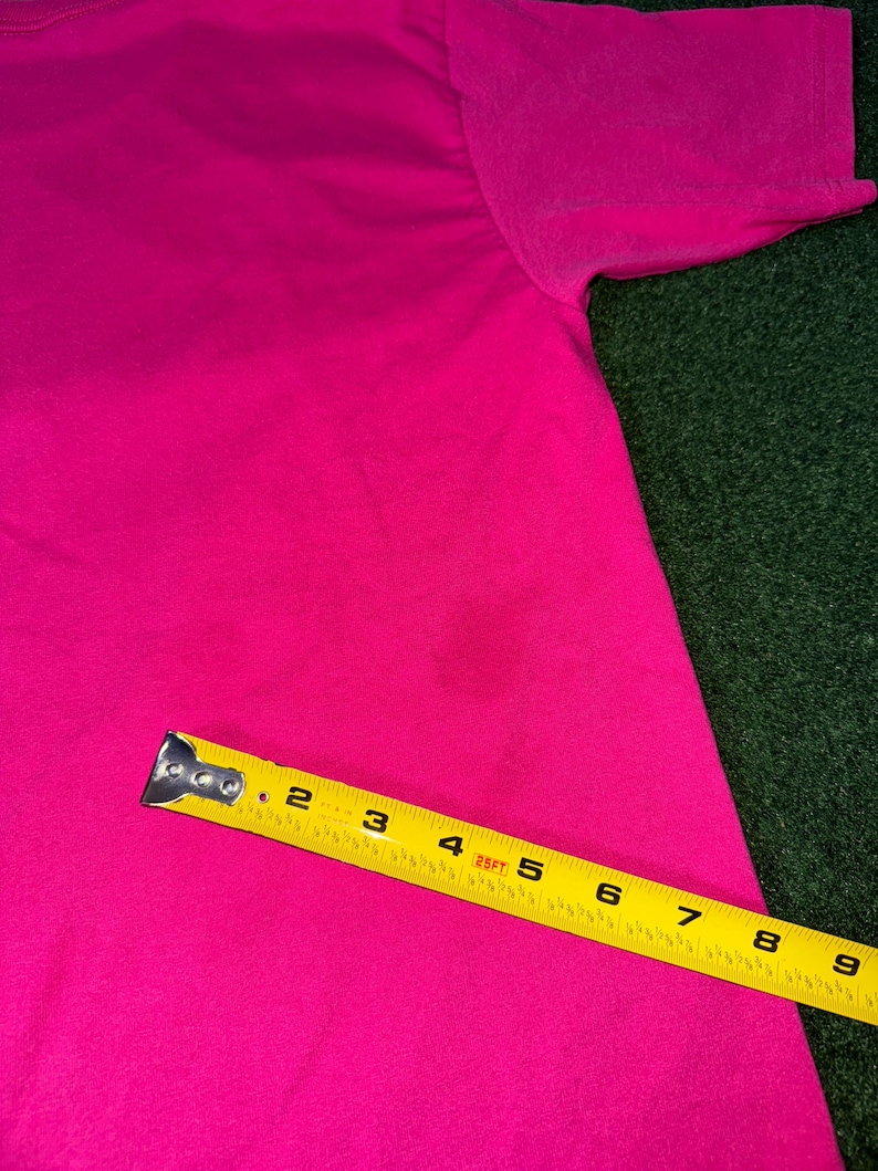 May include: A bright pink t-shirt with a yellow measuring tape placed on top of it. The tape measures 9 inches.