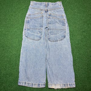 May include: Light blue denim jeans featuring a high-waisted design with a wide-leg silhouette. The garment includes two large, prominent back pockets with metal rivets at the corners and a standard waistband with belt loops and a central button.