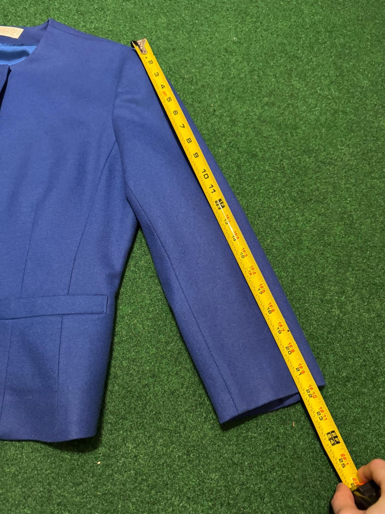 May include: A blue blazer with a notched collar and a single-button closure. The sleeve length is approximately 61 cm. The blazer has a pocket on the left side.