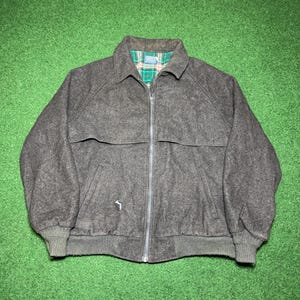 May include: A charcoal gray wool jacket with a full zipper closure. The jacket has a collared neckline and a green, blue, and white plaid lining. The jacket has two front pockets and a ribbed hem and cuffs.