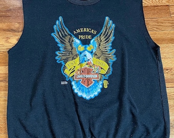 May include: Black sleeveless shirt with a graphic of an eagle holding a Harley Davidson logo. The eagle is surrounded by a banner that reads "America's Pride Est. 1903".