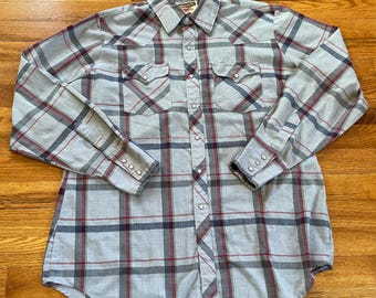 May include: A long-sleeved, light blue plaid shirt with red and gray stripes. The shirt has a button-down collar, a single chest pocket, and two flap pockets on the front. The shirt has a Western-style yoke and a pointed collar.