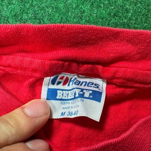 May include: Red Hanes Beefy-T t-shirt tag with white text. The tag says "Hanes Beefy-T 100% Cotton Made in U.S.A. M 38-40".