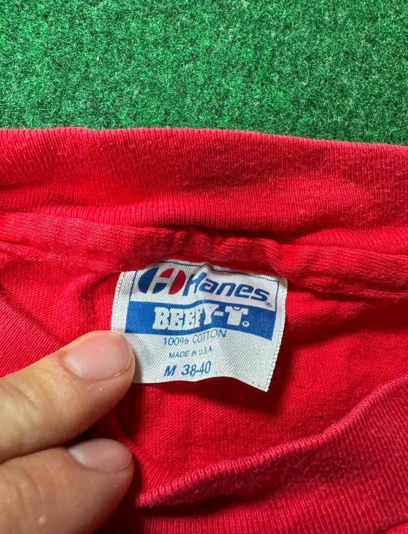 May include: Red Hanes Beefy-T t-shirt tag with white text. The tag says "Hanes Beefy-T 100% Cotton Made in U.S.A. M 38-40".